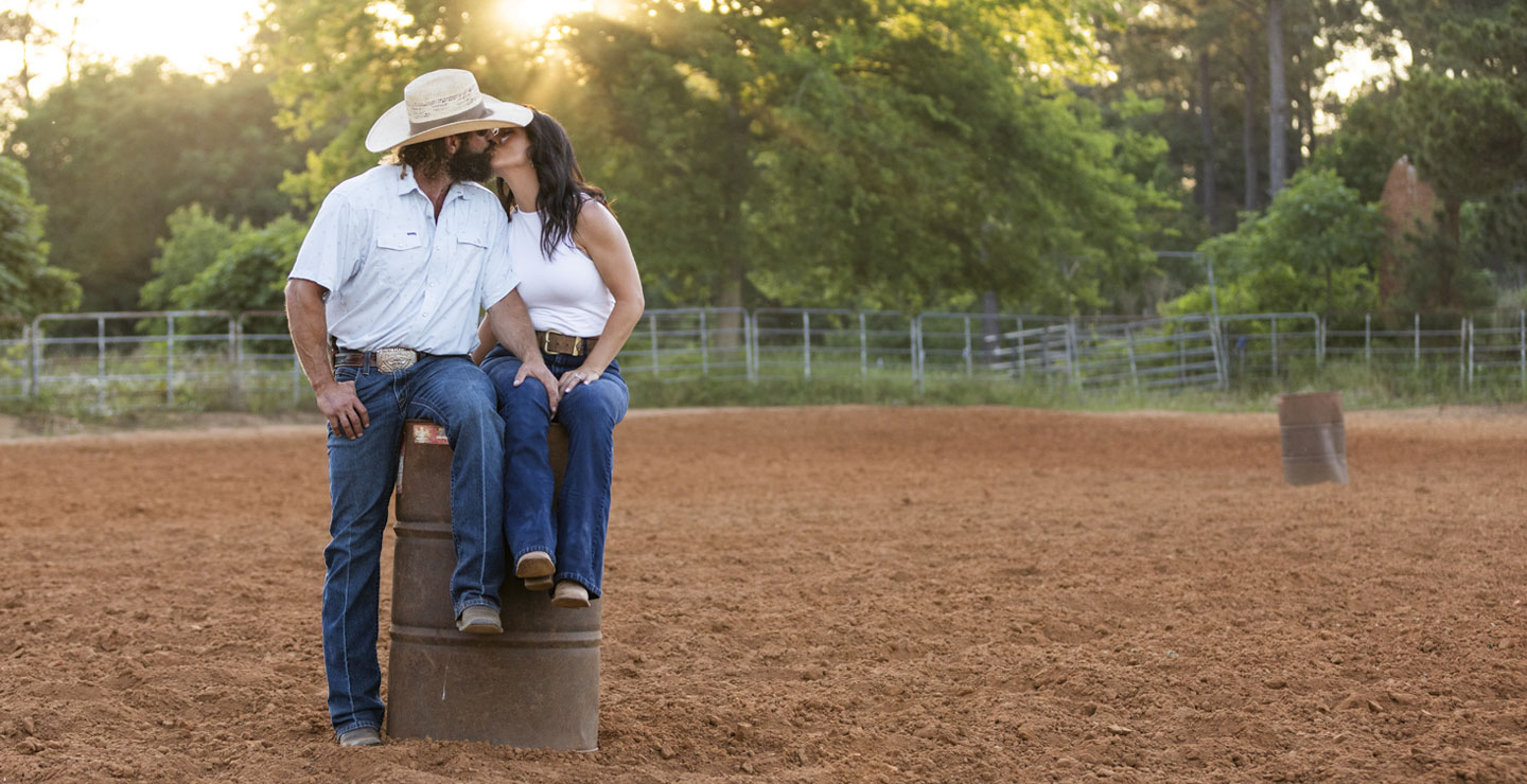 Kip and Kalie Smith sitting on a barrel inside a rodeo arena, kissing.